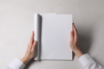 Canvas Print - Woman holding notebook with blank pages at white table, top view. Mockup for design