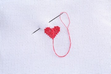 Wall Mural - Embroidered red heart and needle on white cloth, top view