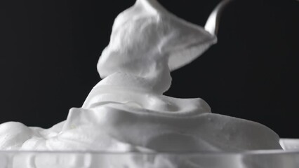 Sticker - Chef takes whipped egg whites with sugar with a spoon from a glass bowl. Close-up of food on a black background, zoom in