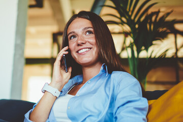 Wall Mural - Positive successful hipster girl calling to customer service for checking account balance on mobile phone while resting with laptop computer indoors, concept of modern technology and communication