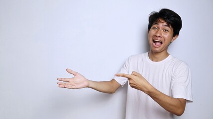 Wall Mural - Excited young Asian man in white shirt with funny expression gesture pointing to open palm