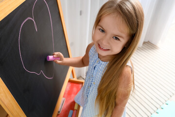 Sticker - Cute little girl drawing on chalkboard at home, closeup