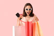 © Pixel-Shot - Young woman with credit card, mobile phone and shopping bags on pink background