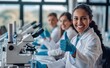 © GreenOptix - A happy female scientist wearing a white lab coat, blue gloves and glasses, modern laboratory, He's giving a thumbs up while smiling