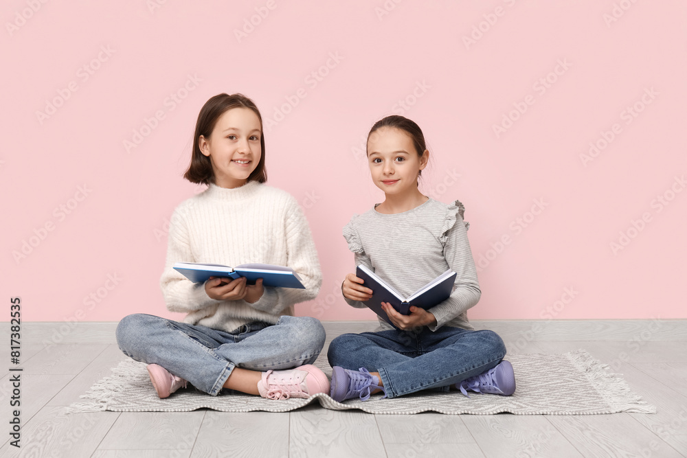 Little children reading books while sitting on floor near pink wall