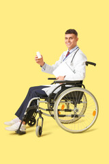 Poster - Young male doctor in wheelchair with laptop and pills on yellow background