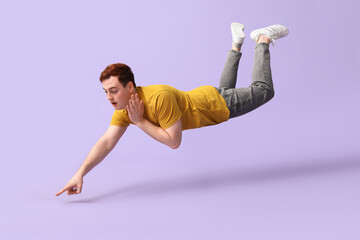 surprised young man flying and pointing at something on lilac background