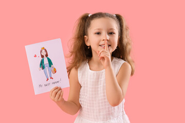 Wall Mural - Cute little girl with card for Mother's Day showing silence gesture on pink background