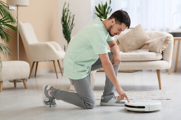 Wall Mural - Young man turning on modern robot vacuum cleaner at home