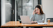 © Satori Studio - A woman is sitting at a desk with a laptop and a cup of coffee. She is talking on the phone and she is in a state of distress