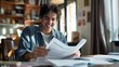 © yj - Happy man smiling while reading and writing documents at home. A happy young male sitting in front of a table with papers, having fun doing his paperwork. generative AI