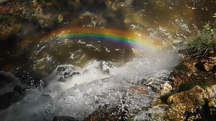 Wall Mural - Crystal clear water tumbling down a rocky cliff with a shimmering rainbow gracefully arching over it.