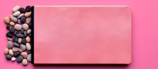 Poster - A pink background with a pebble on it serves as a colorful surface for a top view of a blank notebook with ample copy space