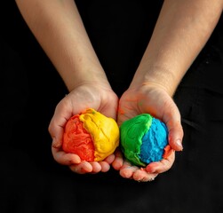 Wall Mural - two hands of child holding colorful play dough, isolated on black background