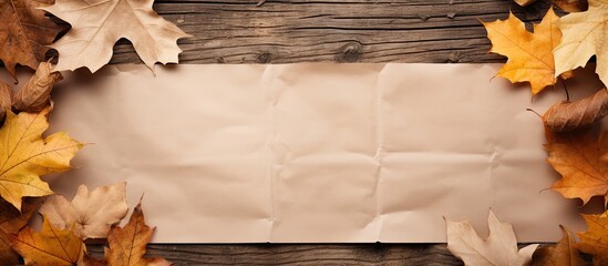 Poster - Top view of a sheet of craft paper surrounded by fallen leaves on a wooden background The image offers copy space for text