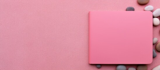 Poster - A pink background with a pebble on it serves as a colorful surface for a top view of a blank notebook with ample copy space