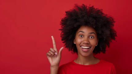 Portrait of beautiful young black woman with an afro hairstyle wearing red t-shirt pointing up on a red background, template for advertising or promotion, with copy space for text