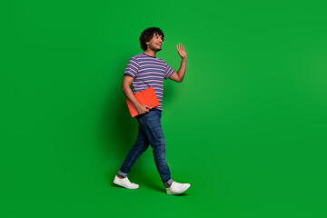 Photo portrait of young senior level programmer indian guy works online using laptop waving hand empty space isolated on green color background