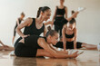 © standret - Woman with pigtail is helping little girl. Group of female kids practicing athletic exercises together indoors