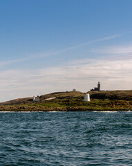 Wall Mural - White lighthouse on a small island with a cloudy blue sky in the background