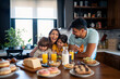 © Dorde - Two happy kids, boy and girl enjoying eating breakfast with parents. Smiling beautiful mother laughing and having fun with her kids and husband during breakfast at home.