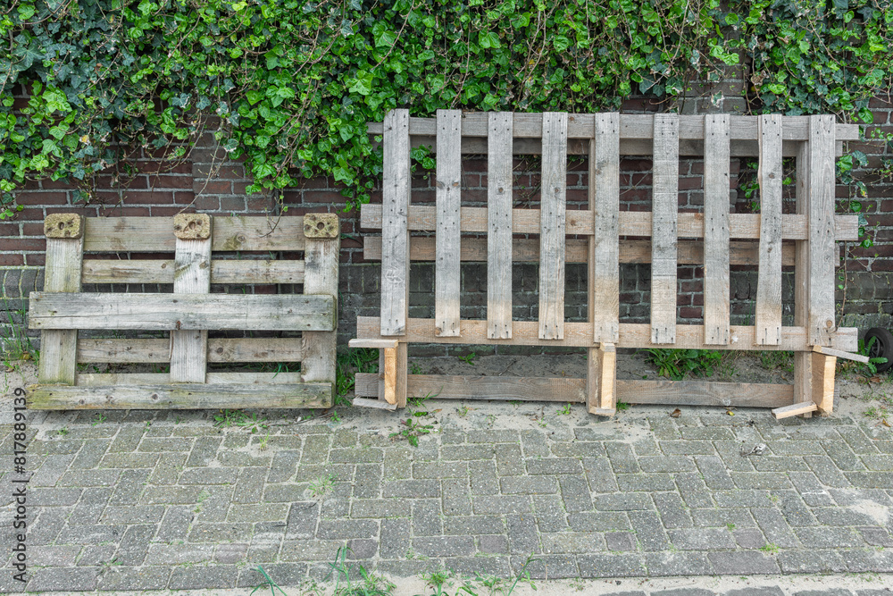 wooden industrial palettes stand outside against a stone wall