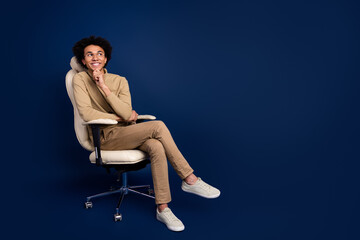 Poster - Full size photo of nice young man sit armchair look minded empty space wear trendy beige outfit isolated on dark blue color background