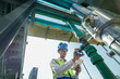 © ultramansk - Male engineer monitoring machinery on a rooftop with city skyline in the background, wearing safety gear