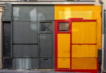 Wall Mural - Paris, France - 05 11 2024: View of typical gray, yellow and red windows shop converted into apartments.