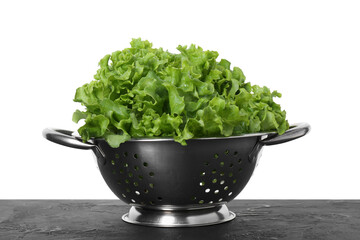 Metal colander with fresh lettuce on black textured table against white background