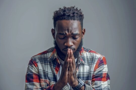 Young african american man praying with hands together, casual clothes, hope expression on face