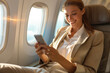 © J S - Happy businesswoman travelling in airplane business class while using smartphone