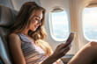 © J S - Young beautiful woman travelling in airplane while using smartphone