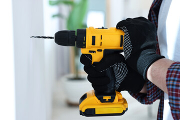 Young handyman working with electric drill at home, closeup