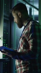 Vertical shot of modern IT engineer using tablet and laptop setting servers in data center while working on mining farm in night