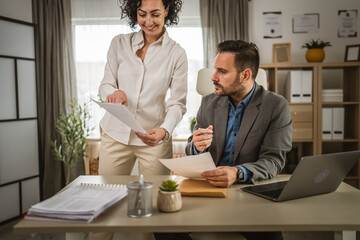 Wall Mural - Two colleagues man and woman hold and read documents at office