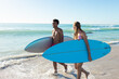 © Wavebreak Media - At beach, diverse couple holding surfboards walking