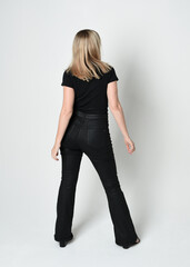 Canvas Print - Full length portrait of beautiful blonde woman wearing modern black shirt and leather pants. Confident  standing pose walking away from camera, silhouetted on white studio background.