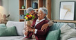 © peopleimages.com - Senior man, flowers and woman on couch for surprise, anniversary and present for birthday in living room. Happy couple, elderly people and plants on home sofa for gift with love, smile and retirement