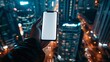 © Mrzproducer - hand holding a smartphone with a blank screen in front of a blurred background of a city at night.