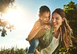 © peopleimages.com - Smile, woman and kid with piggyback in forest for summer, travel holiday and outdoor bonding together. Blue sky, happy and mother with girl in park for child development, support or love on adventure