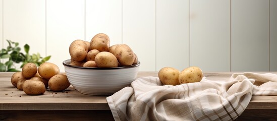 Poster - The table is adorned with a bowl containing fresh pristine potatoes A kitchen towel complements the arrangement Ample copy space image