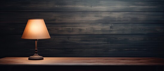 Poster - Dark room with a wooden table featuring a glowing lamp providing ample copy space image