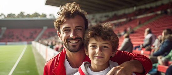 Poster - A cheerful sports enthusiast and his son proudly donning the jerseys of their beloved team pose for a photo at a soccer game gazing directly into the camera Copy space available