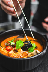 Poster - A chef’s hand garnishing a bowl of seafood soup with herbs, capturing the motion and precision in food presentation