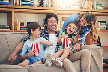 Canvas Print - Happy family, watching tv and laughing with popcorn for funny movie, weekend or holiday on living room sofa at home. Mom, dad and young children with smile for comedy or streaming service at house