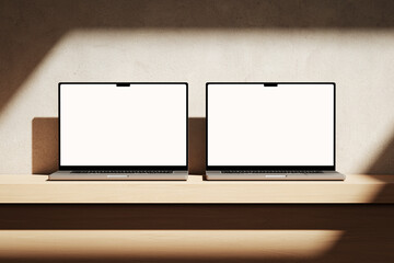 Two Apple MacBooks Pro on the wooden desk on a plaster background