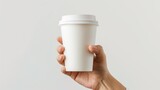 A hand holding a white paper coffee cup with a white lid against a pale grey background.