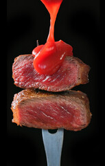 Wall Mural - two pieces of freshly grilled beef steak meat and pouring tomato sauce isolated on black background; selective focus