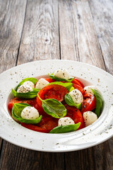 Wall Mural - Caprese salad - tomatoes and mozzarella balls served in white bowl on wooden background
